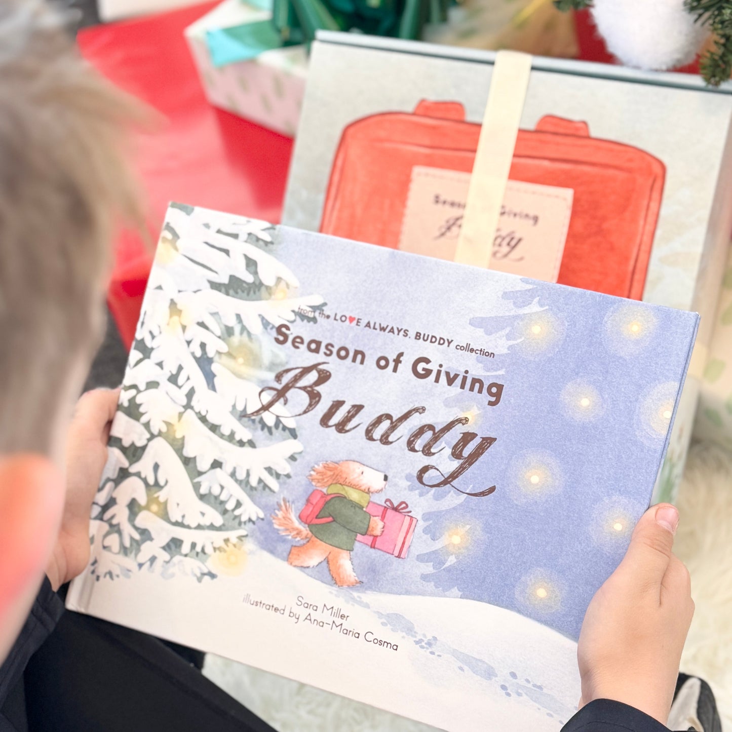 Child holding a book titled 'Season of Giving Buddy' with a Christmas-themed background.